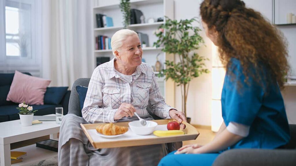 Older adult using a walker while practicing a supervised hallway walk with a caregiver.