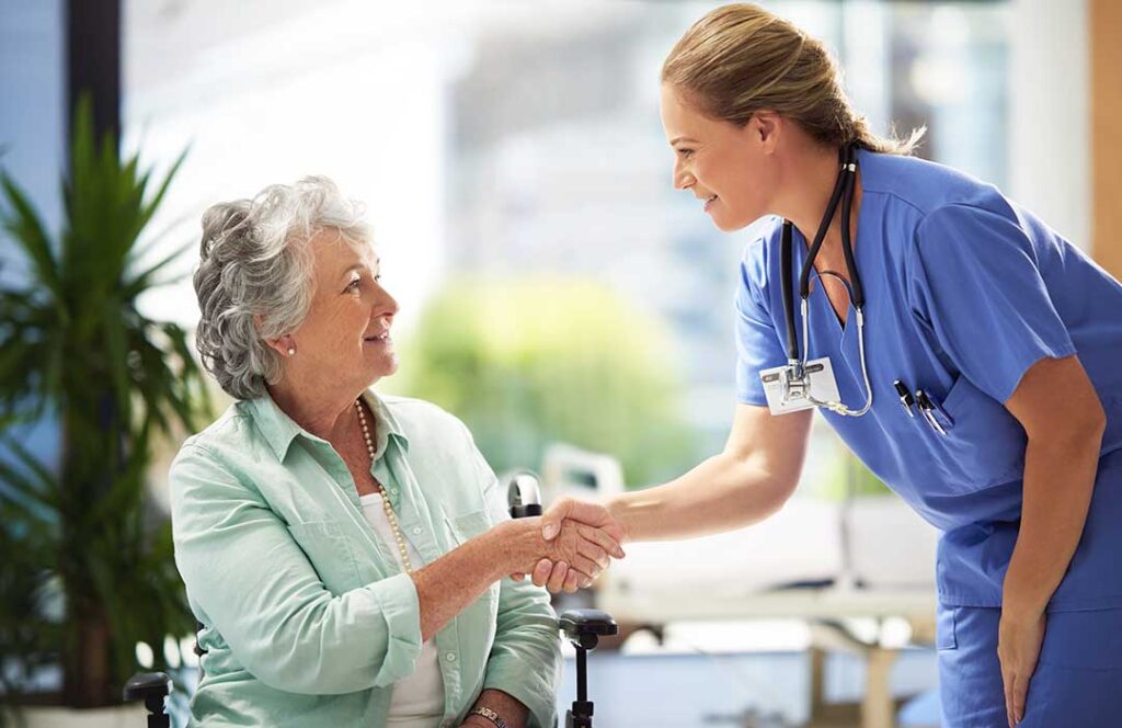 Caregiver helps an older resident sanitize hands in a bright assisted living common area.