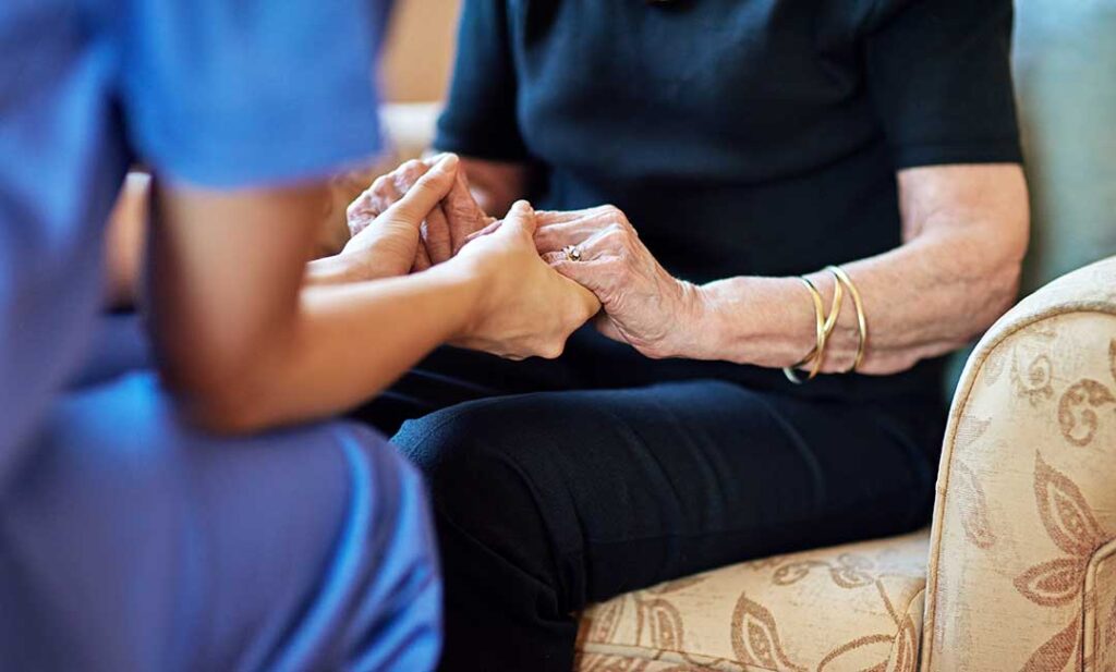 Two seniors and a caregiver sitting at a table, coloring together in a bright, home-like common room.